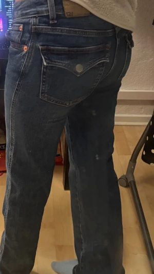 Mörkblå raka jeans med fickdetaljer - Snygga mörkblå jeans med raka ben och klassisk ficksdesign. Jeansen har dekorativa bakfickor med lock och knapp samt kontrastsömmar. Tillverkade i denim med en autentisk tvätt. Perfekta för en avslappnad och trendig look.