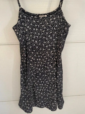 Blommig kort klänning Trend Report - Söt kort klänning från Trend Report i marinblått med små vita blommor. Klänningen har smala axelband och ärmlös design, perfekt för varma dagar. Lätt och bekväm passform som ger en avslappnad men ändå stilren look.