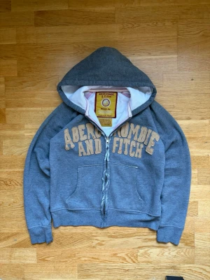 Grå hoodie från Abercrombie & Fitch - Abercrombie & Fitch Hoodie - Y2K / 2000-tal - Grå - Herr - Strl M Klassisk grå hoodie från Abercrombie & Fitch med äkta Y2K/2000-talskänsla. En tidlös modell som passar perfekt för både vardag och en avslappnad streetwear-look. Märke: Abercrombie & Fitch Storlek: Medium (M) V Färg: Grå V Stil: Y2K / 2000-tal / Vintage V Passar: Herr (kan även bäras oversized) Hoodien är i fint begagnat skick med normalt slitage för sin ålder. Ett perfekt val för dig som gillar vintage, Y2K-mode eller klassiskt 