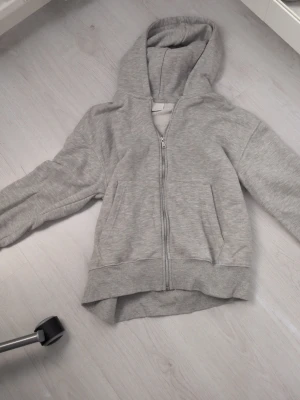 Grå zip hoodie från Zara - Säljer en enkel och stilren grå hoodie från Zara med dragkedja framtill och två fickor. Hoodien har ribbade muddar vid ärmslut och nederkant samt en stor huva. Perfekt för chill dagar eller till skolan.