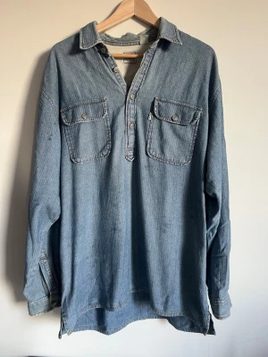 Blå denim henley-skjorta från Levi's - Säljer en blå henley-skjorta i denim från Levi's med två bröstfickor och knappdetaljer framtill. Skjortan har lång ärm och avslappnad passform, perfekt för en chill och stilren look. Klassisk krage och snygga sömmar.