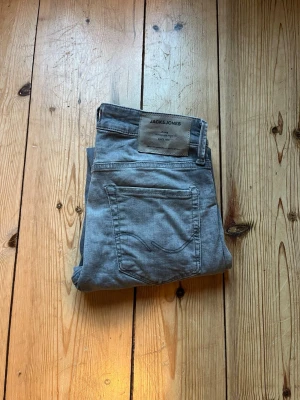 Grå jeans från Jack & Jones - Säljer snygga grå jeans från Jack & Jones med klassisk femficksdesign och raka ben. Jeansen har en patch med logga bak i midjan och är gjorda i mjukt denimtyg. Perfekta för en avslappnad och stilren look. Hör av dig vid frågor🙌🏼