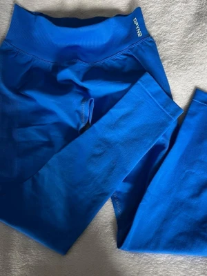 DFYNE Impact Leggings - Snygga blå seamless leggings från DFYNE med hög midja och stretchigt material. Perfekta för träning eller chill. Diskret logga vid linningen och mjuk, följsam passform som sitter skönt hela dagen. Storlek S