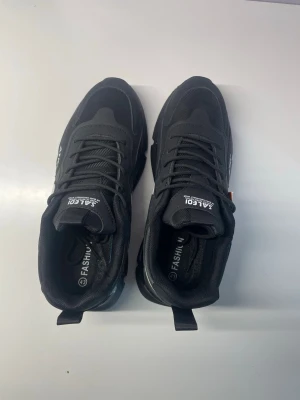 Svarta sneakers - Oanvända skor p.g.a att dem är för små. Snygga svarta sneakers med vit sula och vit swoosh på sidan. Skorna har textdetaljer och är tillverkade i en mix av mesh och syntetmaterial. 