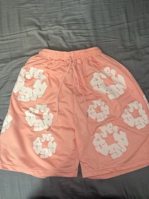 Rosa Denimtears shorts.  - Säljer ett par ljusrosa shorts med elastisk midja och snörning. Shortsen har stora vita blommönster tryckta över hela plagget och en bakficka. Perfekta för sommaren och riktigt sköna att bära. Pris kan diskuteras vid snabb affär.