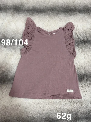 Ljuslila topp med spetsärmar - Söt ljuslila topp med ärmlös design och volangprydda spetsärmar. Perfekt för varma dagar och enkel att matcha med olika outfits. 🌸 Fint använt skick. Storlek 98/104