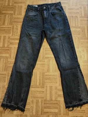 Svarta raka jeans med rå kant - Säljer ett par svarta raka jeans med fransig, rå kant längst ner på benen. Jeansen har klassisk femficksmodell och är tillverkade i denim. Perfekta för en avslappnad och trendig look.