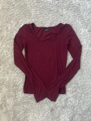 Mörkröd långärmad topp - En enkel och stilren mörkröd långärmad topp med rundad urringning. Toppen är tight i modellen och passar perfekt till jeans eller kjol. Tillverkad i mjukt material som känns skönt mot huden.