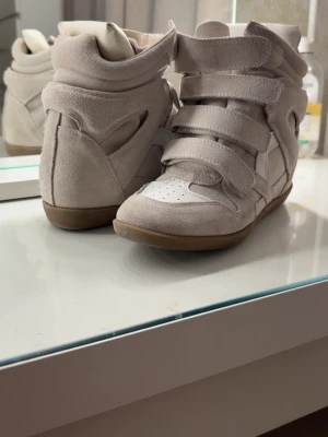 Beige Isabel Marant - Säljer ett par ikoniska beige Isabel Marant i 38 men passar även 37 och 39. Skorna är i mocka och textil med ljusbrun sula och vita detaljer. Köpte för 7000kr på deras hemsida. Om du har några frågor så är jag öppen för allt, även prissänkning!💕