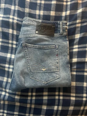 Replay jeans  - Säljer ett par blå jeans från Replay med snygga slitningar och hål på båda knäna. Jeansen har klassisk femficksmodell, normal midja och raka ben. Perfekta för en avslappnad och trendig look. OBS HÅL i flickan! Storlekslapp saknas med bedöms till 33/32 JAG SKICKAR EJ FLER BILDER PÅ JEANSEN! för storleksguide hänvisar jag till måtten och för bättre inblick i passformen rekommenderar jag att googla på modellnamnet.JAG TAR EJ EMOT RETURER. kom ej med bud om du ej köper efter:)