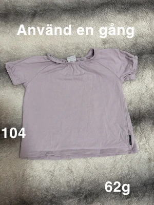 Ljuslila kortärmad t-shirt - Säljer en söt ljuslila t-shirt med korta ärmar och rund hals. T-shirten är enkel i modellen och har en liten etikett nertill på sidan. Perfekt för en avslappnad stil.🌸 Använd en gång. Storlek 104. 