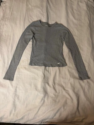 Grå långärmad topp - Säljer en enkel och stilren grå långärmad topp med rund hals. Toppen har en tight passform och är tillverkad i ett mjukt material som känns skönt mot huden. Perfekt att matcha med jeans eller kjol för en clean look.