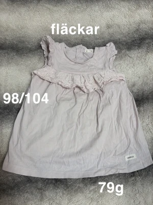 Ljuslila ärmlös topp med volang - Ljuslila topp med volang och broderad spetsdetalj över bröstet. Ärmlös modell med små volangärmar och rund hals. Perfekt för en söt och enkel stil till sommaren.🌸 Fläckar. Storlek 98/104