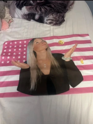 Bild med rosa USA-flagga och tryck - Bild med rosa och vita ränder samt stjärnor i USA-flagga-stil. Tryck av en tjej med långt blont hår och emojis. Dragkedja upptill. Perfekt för smink eller småprylar.