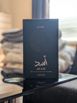 Lattafa Asad Elixir (100 ml) - Säljer Lattafa Asad Elixir (100 ml) i absolut nyskick med box, endast testsprayad.  En extremt kraftfull och maskulin doft med grym prestanda som håller hela dagen. Doften påminner stilmässigt mycket om originalet med sin mörka, rika och exklusiva karaktär.  Den öppnar med kryddiga noter av saffran och svartpeppar, för att sedan landa i en otroligt len, varm och krämig bas av vanilj, trä och bärnsten. Perfekt för utekvällar för dig som vill ha en doft med tung karaktär!