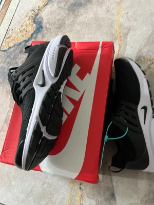 Nike presto - Snygga svarta Nike sneakers med vit sula och svart swoosh. Ovandelen är i mesh för bra andningsförmåga och har plastdetaljer vid snörningen. Skorna har en sportig look och passar perfekt till streetwear-stilen.
