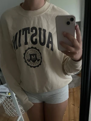 Beige sweatshirt med Austin-tryck - Säljer en beige oversized sweatshirt med svart texten 'AUSTIN' och ett tryck framtill. Tröjan har rund halsringning, långa ärmar och ribbade muddar vid ärmslut och nederkant. Perfekt för en avslappnad och trendig look.
