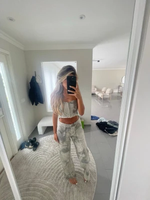 Grått mönstrat bustier-set jumpsuit - Säljer ett trendigt tvådelat set med bustier-topp och matchande byxor i grått och vitt mönster. Toppen har markerade sömmar och raka axelband, medan byxorna är raka och höga i midjan. Perfekt för dig som gillar en edgy och modern stil.