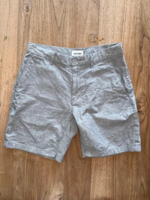 Ljusgråa shorts från East West - Snygga ljusgråa shorts från East West. Klassisk modell med fickor fram och bak, bälteshällor och knappstängning. Perfekta för varma dagar och ger en clean och avslappnad look. Storlek 29”