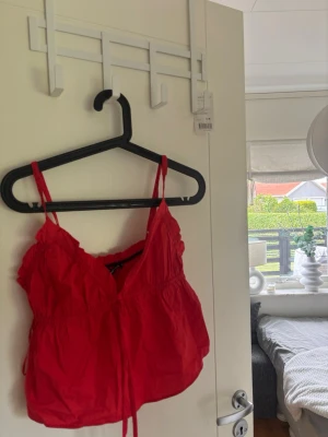 Röd croppad linnetopp med snörning - Snygg röd croppad linnetopp med tunna axelband och snörning framtill. Toppen har en luftig passform och är perfekt för varma dagar. Passar till både jeans och kjol för en trendig look.
