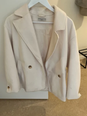 Ljusbeige kappa från Urban Outfitters - Stilren ljusbeige kappa från Ginatricot med dubbelknäppning och breda slag. Kappan har två fickor framtill och är tillverkad i ett mjukt, ull-liknande material. Perfekt för dig som gillar minimalistisk och trendig stil. Nypris 699 slutsåld säljer för 400 