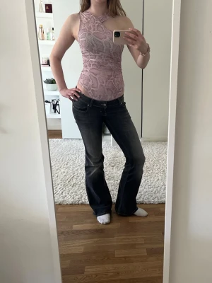 Rosa ormmönstrad body med omlott - Säljer en snygg rosa body med ormmönster och omlottdetalj över axeln. Bodyn har ärmlös design och smickrande passform. Materialet är stretchigt och mjukt, perfekt för att skapa en trendig look. Helt ny med lapp kvar.