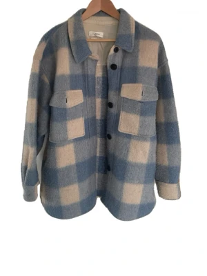 Isabel Marant kappa  - Kappa från Isabel Marant i mjukt ullmix-tyg med stora blå och beige rutor. Två bröstfickor med lock och knappar framtill. Avslappnad passform och klassisk krage. Perfekt lager-på-lager-plagg för en trendig look. Pris kan diskuteras!