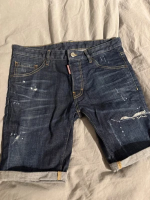 Mörkblå jeansshorts från Dsquared2 - Säljer ett par mörkblå jeansshorts från Dsquared2 16y men sitter som 44or. Mest legat i garderoben.