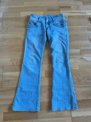Ljusblå bootcut jeans från BAY - Säljer ett par ljusblå bootcut jeans från BAY med klassisk femficksmodell och dubbla knappar i midjan. Jeansen har utsvängda ben och är tillverkade i mjuk denim. Perfekta för en avslappnad och trendig look.