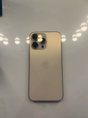 Guld iPhone 14 Pro Max - Snygg iPhone 14 Pro Max i guld med elegant glasbaksida och rostfria kanter. Telefonen har tre stora kameror på baksidan och en stilren, modern design med rundade hörn och stor skärm. Perfekt för dig som vill ha en kraftfull och lyxig mobil.