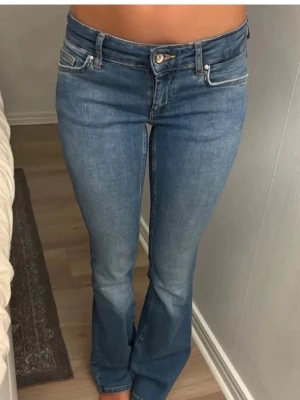 Blå bootcut jeans från Only - Säljer ett par klassiska blå bootcut jeans från Only. Jeansen har låg midja, fem fickor och snygga sömmar. Materialet är stretchigt denim som sitter bekvämt och formar sig efter kroppen. Perfekta för en trendig och avslappnad look.