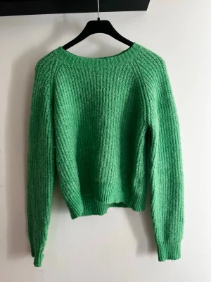 Grön stickad tröja från Lindex - Snygg grön stickad tröja från Lindex i storlek 170. Tröjan har en klassisk rund halsringning, långa ärmar och ribbstickade muddar. Materialet är mjukt och fluffigt, perfekt för att hålla värmen under kyliga dagar. Aldrig använd.