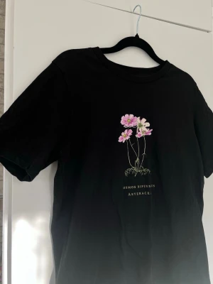Svart t-shirt med rosa blommor från Gina Tricot, stl S  - Säljer en svart t-shirt med fina rosa blommor 🌷 Sparsamt använd. Sömmen längst ner har lossnat lite i en av maskorna, se bilder. 