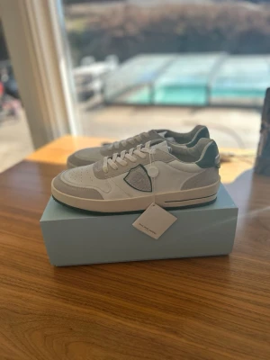 OANVÄNDA Philippe Model Herrskor 43 Grön/Vit  - Snygga sneakers från Philippe Model i vitt läder med gröna detaljer och yttersula, perfekta inför våren. Skorna har aldrig haft en fot i sig, aldrig klivit ett steg, sprillans nya som ni kan se på den andra bilden. De är självklart äkta och kvitto ingår. Antingen kan ni hämta dem i sollentuna eller så kan jag frakta de med köparskydd. Storleken är 43, är något större i passform. nypris ligger på 3000kr, mitt pris endast 1349kr.