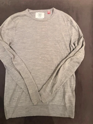 Ljusgrå merinoulltröja Kronstadt - Säljer en stilren ljusgrå stickad tröja från Kronstadt i extra fin merinoull. Tröjan har rund halsringning, långa ärmar och en klassisk, enkel design som passar till det mesta. Perfekt för dig som gillar minimalistisk och skandinavisk stil.