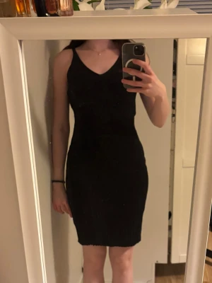 Svart ärmlös ribstickad klänning - En ribstickad och svart kortklänning med v-ringning både bak och fram. Klänningen är stretchig och har smala axelband. 