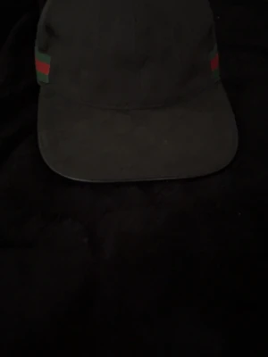 Svart keps  - Snygg svart keps  med klassiska röd-gröna ränder på sidorna. Kepsen har böjd skärm och justerbar passform. Säljer den för att det inte är min stil längre. Några frågor eller funderingar hör av dig. :)