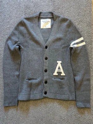 Abercrombie & Fitch Stickad Cardigan - Säljer denna feta Abercrombie & Fitch stickad cardigan | Mycket bra skick | Storlek M | Längd ≈ 70cm , Bredd armhåla - armhåla ≈ 49-50cm | Model 175cm, 70kg | Hör av vid funderingar, pris kan diskuteras!