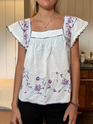 Vit blus med broderade blommor - Söt vit blus med broderade blommor i rosa och blått. Den är från Hoss Intropia i marbella storlek S🩷