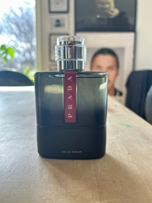 Prada Eau de Parfum carbon 100 ml - Snygg parfym från Prada i en stilren svart glasflaska med silverfärgad kork och röd etikett framtill. Flaskan har en modern, fyrkantig form och känns lyxig och elegant. Perfekt för dig som gillar exklusiva dofter och vill ha en parfym som sticker ut i badrumshyllan.