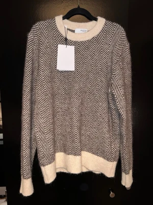 Selected Homme alpaca stickad tröja - Säljer en stickad tröja från Selected Homme med svartvitt fiskbensmönster. Tröjan har rund halsringning och ribbade muddar i beige vid ärmslut och nederkant.
