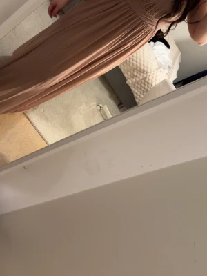 Beige långklänning med omlottliv - Säljer en elegant beige långklänning med omlottdetalj över bysten och plisserad kjol. Klänningen har smala axelband och ett mjukt, flytande tyg som ger en snygg siluett. Perfekt för dig som vill ha en stilren och trendig look.