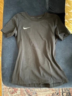 Svart Nike t-shirt  - Svart t-shirt från Nike i dry-fit material. Perfekt för träning eller chill. Liten deo fläck (som inte har gått bort än från tvätten) på högra sidan, men den synns knappast. Barnstorlek M men hade sagt att den passar XS-S. 
