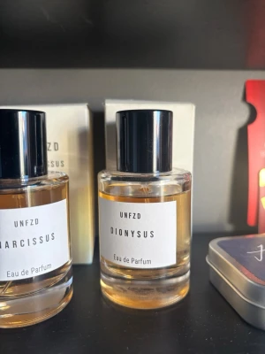 UNFZD Dionysus Eau de Parfum annars kostar ny 970kr! - UNFZD Dionysus Eau de Parfum i en stilren, rund glasflaska med svart lock. Doften har en elegant och minimalistisk design med vit etikett och tydlig text. Perfekt för dig som gillar exklusiva och moderna parfymer.