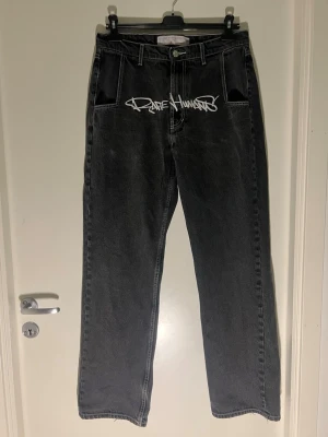 Svarta jeans från Rare Humans - Säljer ett par svarta raka jeans från Rare Humans med vit graffiti-liknande logga framtill och unik brodyr vid benslutet. Jeansen har gylf, klassiska fickor och är gjorda i kraftig denim (säljs inte längre). De har slitage vid benöppning och hade ett hål i skrevet som jag sydde ihop (se näst sista bild).   Midjemått: 41 cm Totallängd: 120 cm                                                           Benöppning: 22 cm