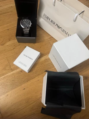Emporio Armani silver/svart klocka - Stilren klocka från Emporio Armani med svart urtavla och silverfärgad länk i metall. Klockan har flera små urtavlor och klassisk design. Levereras med originalask, manual och Emporio Armani-påse.