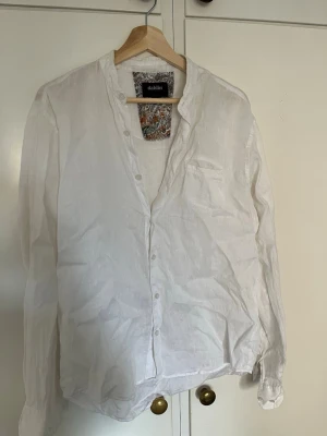 Vit linneskjorta från dahlin - Säljer en vit henley-skjorta från dahlin i luftigt linne. Skjortan har knappar framtill, lång ärm och en liten bröstficka. Perfekt för dig som gillar en avslappnad och stilren look.