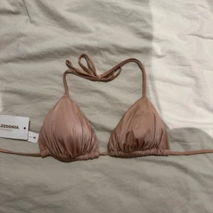 Beige bikiniöverdel från Calzedonia - Säljer en rosa trekantsbikini från Calzedonia med knyt i nacken och ryggen. Bikinin har en stilren och enkel design i mjukt material som ger en snygg passform. Perfekt för lata dagar på stranden eller vid poolen.