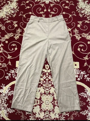 Grå H&M Kostymbyxor - Snygga grå kostymbyxor med raka ben. Byxorna har bälteshällor och två bakfickor för en clean look. Perfekta till skjorta eller t-shirt för en stilren outfit. 2 för 150 kr på alla dambyxor!