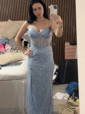 Ljusblå glittrig långklänning - Vid intresse skriv privat! Säljer en ljusblå lång balklänning med tunna axelband och glittriga paljettdetaljer. Klänningen har en figurnära passform, transparenta partier upptill och v-ringad urringning. Klänningen har en slits eller vad man säger. 